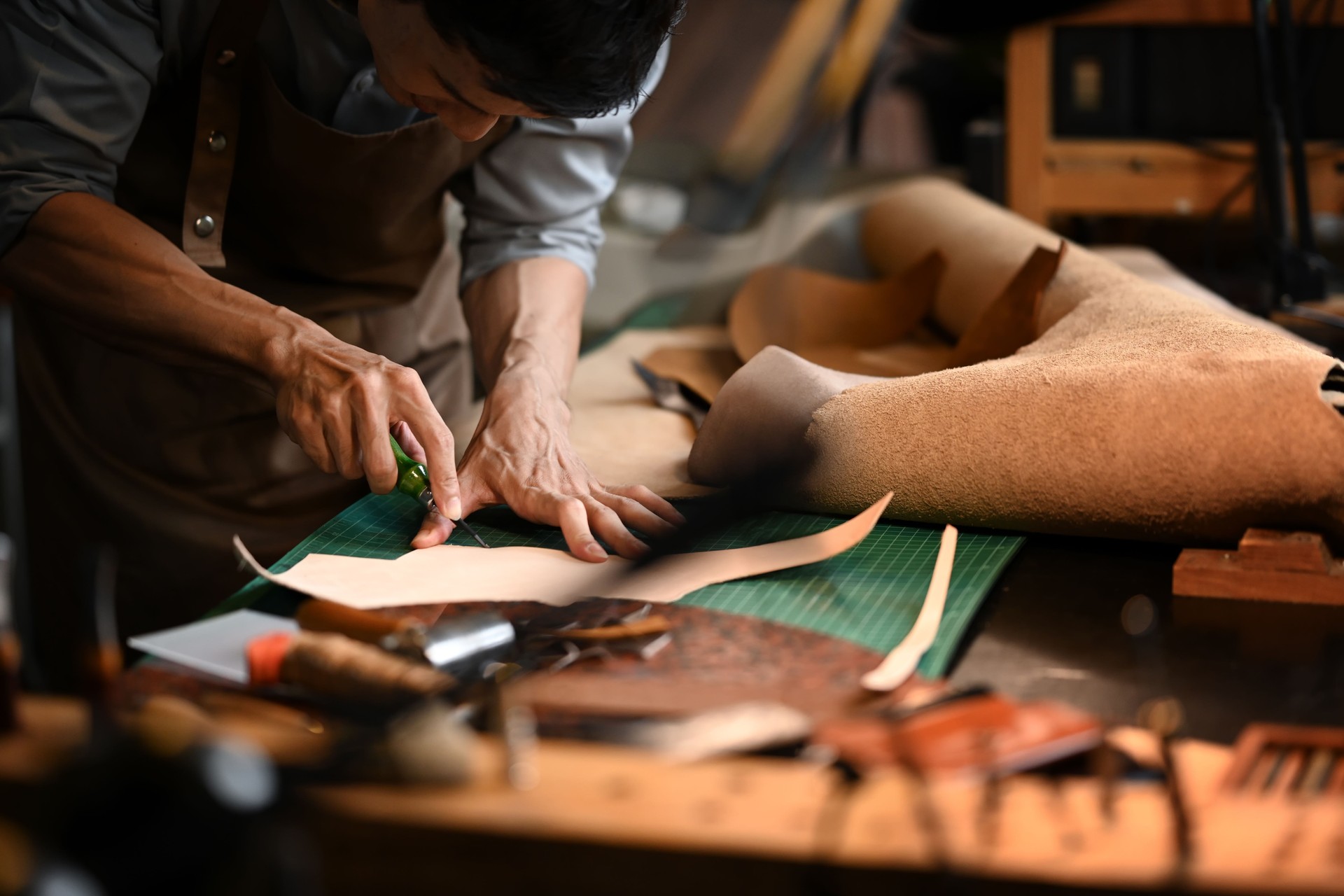 Concentrated of shoemaker cutting brown leather patterns in atelier workshop. Handmade concept