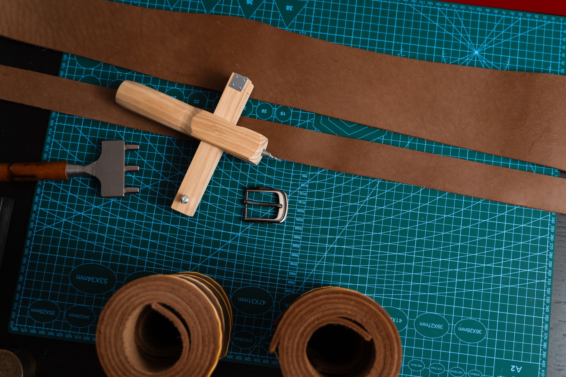 Leathercraft tools and belt-making preparation. Leatherworking setup featuring tools, buckle, and leather strips laid out neatly on a mat, ready for belt making.